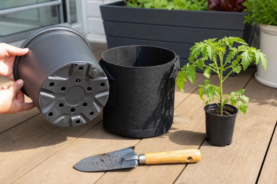 An empty 5-gallon fabric pot and a plastic planter showing drainage holes on a deck.